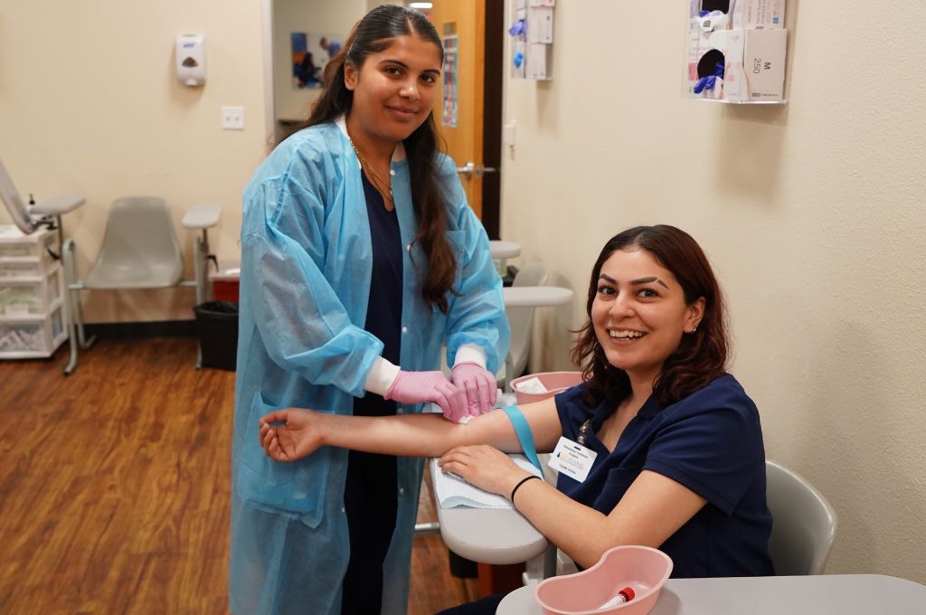 Phlebotomy training students smile as they practice blood draws.