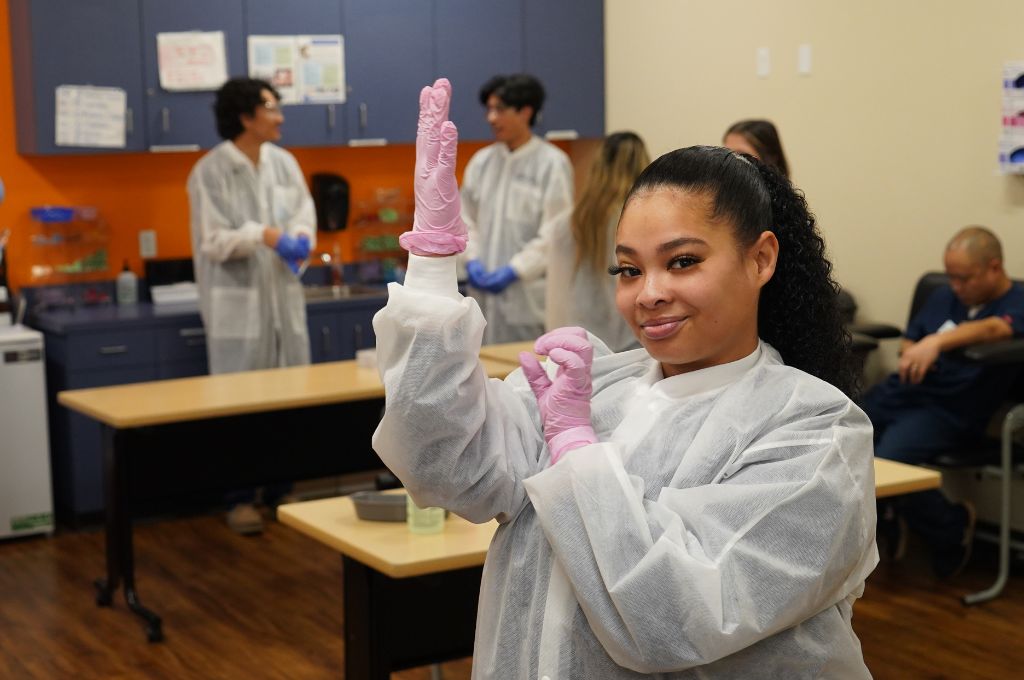 A phlebotomy tech student puts on gloves.