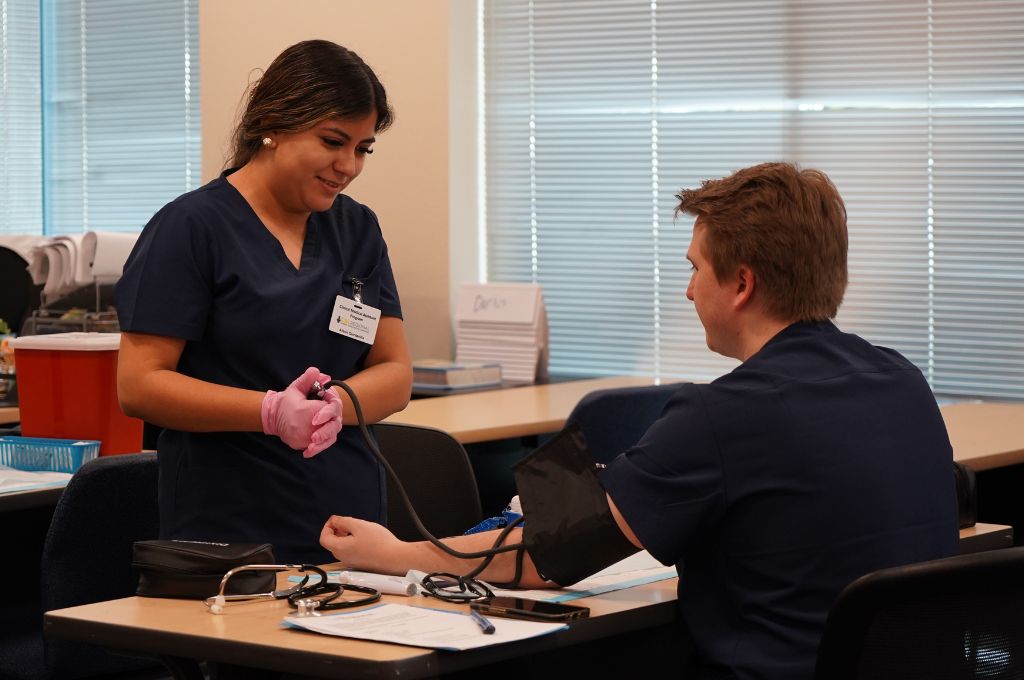 Student practicing blood pressure measurement during hands-on training, illustrating a key clinical duty in the medical assistant job description.