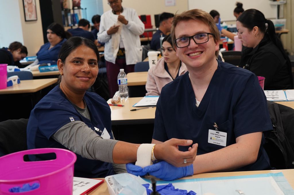 Two students in a clinical classroom setting practicing bandaging techniques, a hands-on skill commonly found in the medical assistant job description.