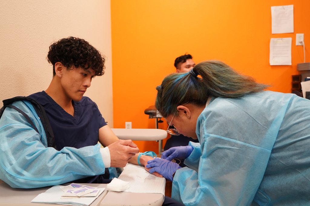 Student practicing a venipuncture procedure in a phlebotomy training lab.