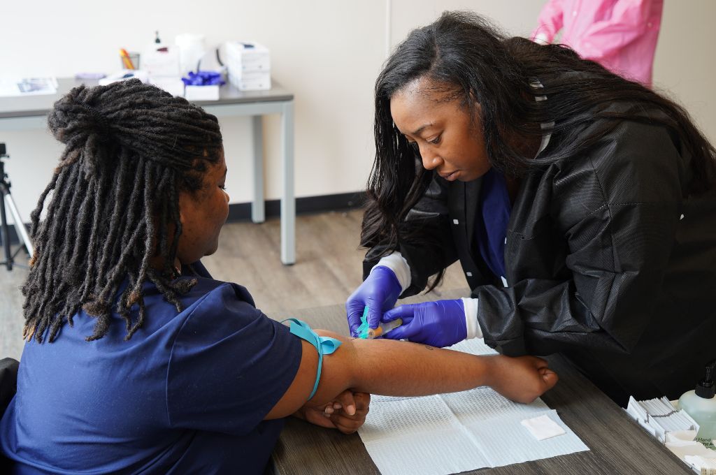 Phlebotomy student practicing a blood draw during hands-on training at a vocational healthcare program