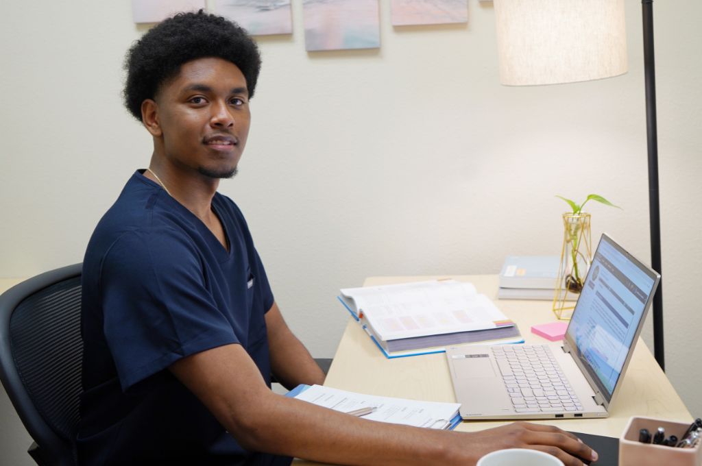 Student in scrubs studying at a desk with a laptop and textbooks for an online medical billing and coding program in Texas