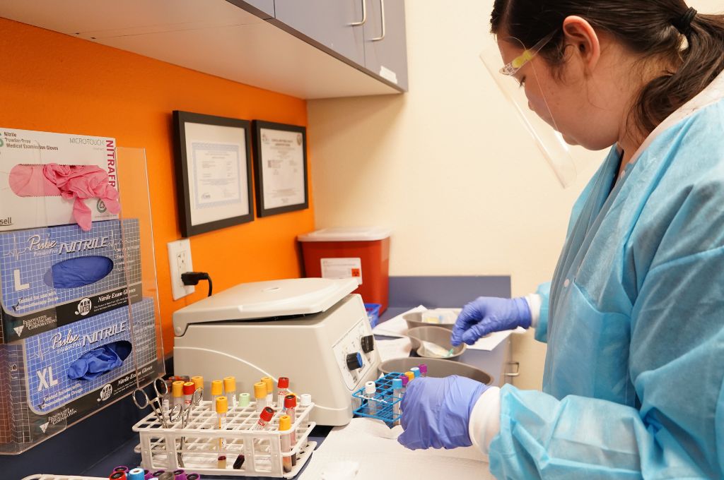 Phlebotomy student processing blood specimens in a lab using a centrifuge during hands-on training
