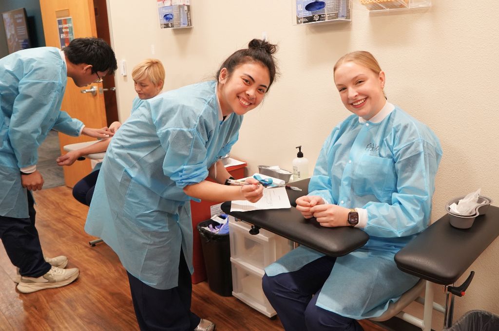 Phlebotomy students practicing venipuncture technique together during clinical lab training